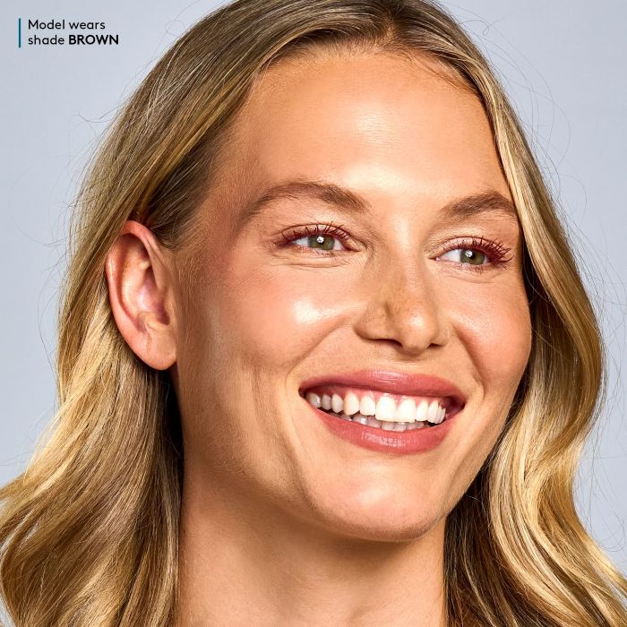 Close-up of a model with blonde hair and Colorescience Total Lash Mascara in Brown on a neutral background